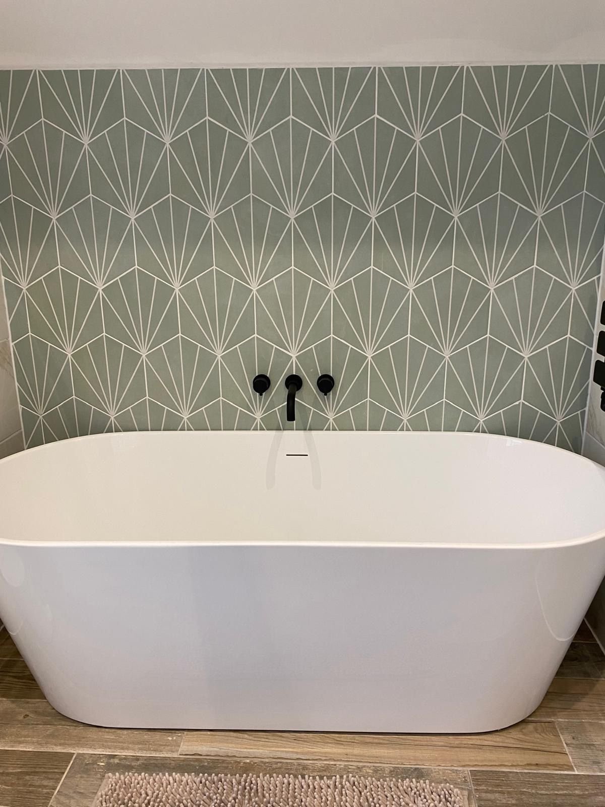 A freestanding bath against a green tiled wall