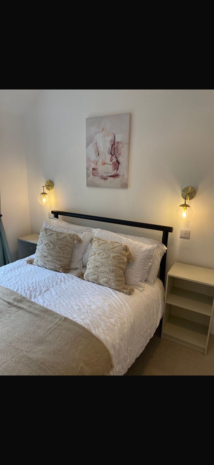 A made-up double bed with wall lights either side