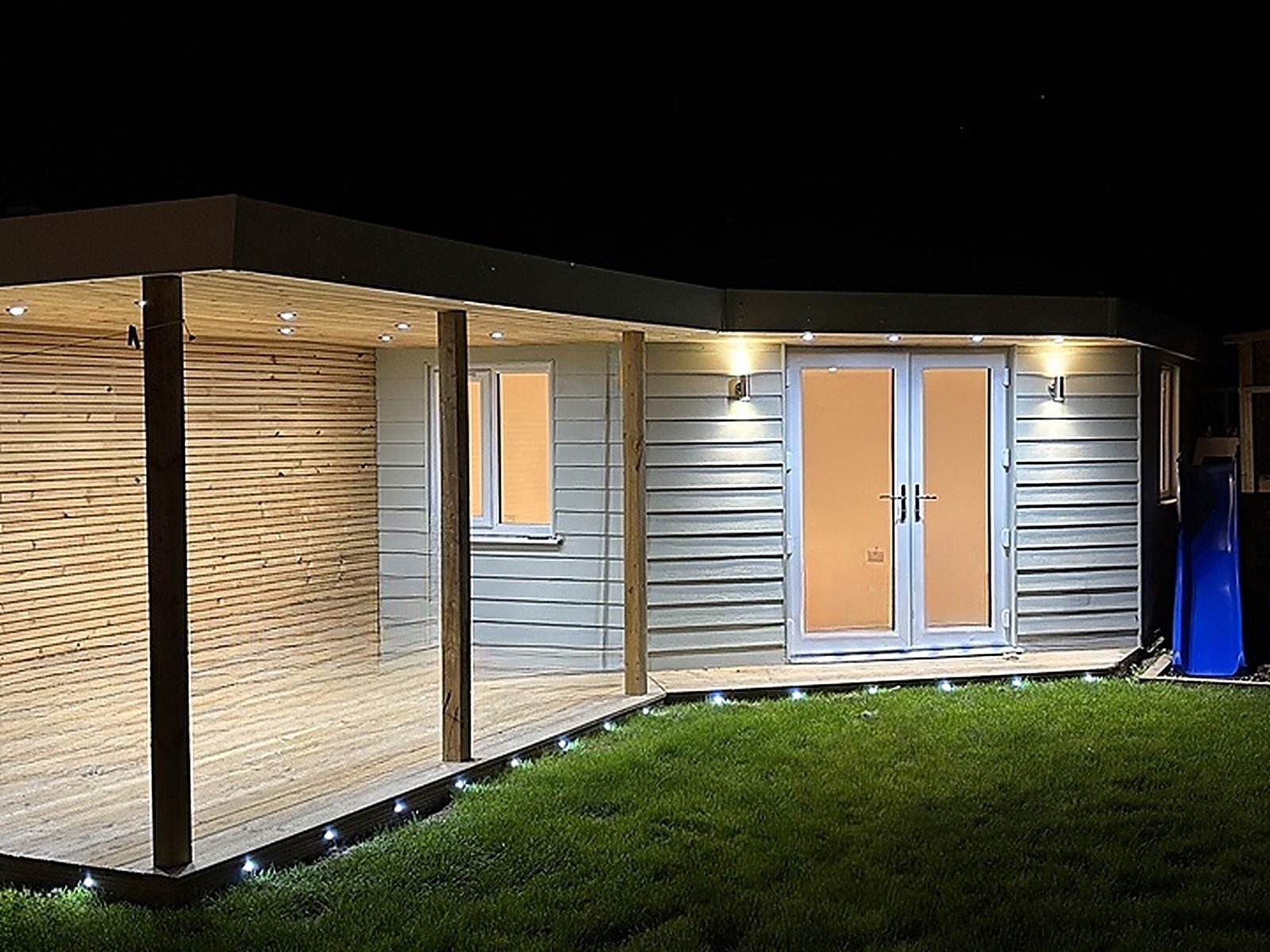 A garden room with a covered veranda lit up at night